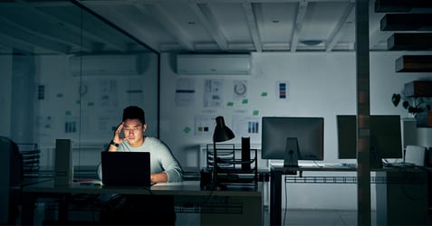 an image of a tech employee appearing stressed working late on his laptop at the office
