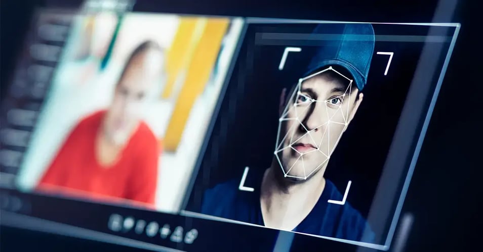Man looking at camera on a computer screen while facial recognition software maps geometric tracking points across his face, illustrating AI-powered deepfake technology and digital identity impersonation during a video call.