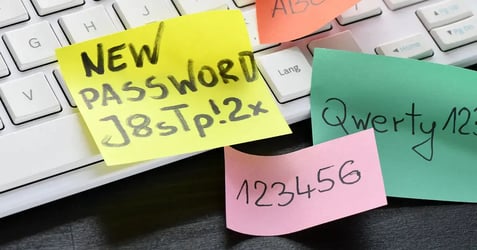 Sticky notes with weak passwords on a keyboard, illustrating common examples of cybersecurity risks caused by poor employee credential management.