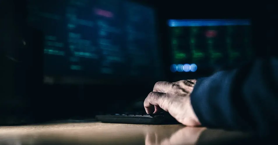 Close-up of a person coding on blurred monitors, illustrating efforts to manage dark data risks.