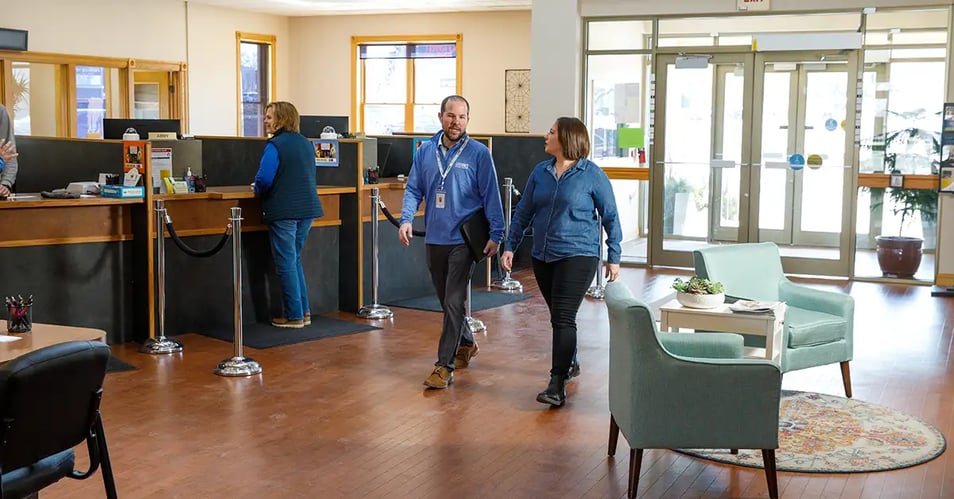 Bright community bank lobby with two professionals walking near teller stations