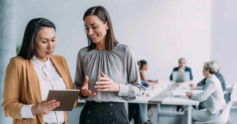 Two professionals collaborating over a tablet in a modern bank office, discussing how managed IT services for banks support their team.