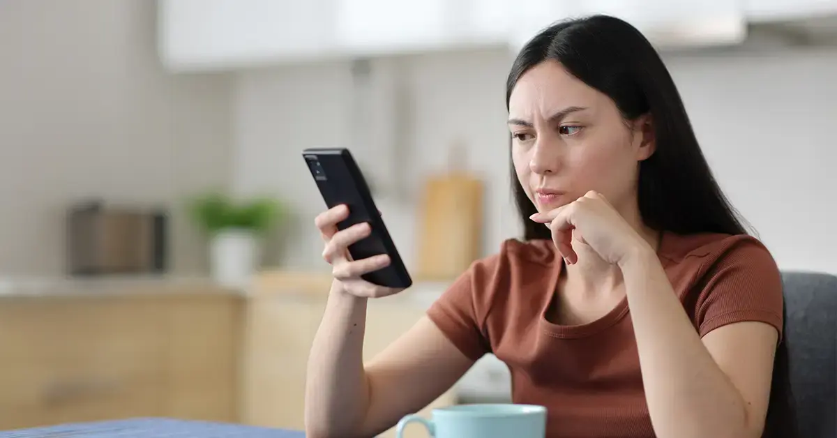 an image of a young woman looking at her phone questionably while listening to a possible vishing scam