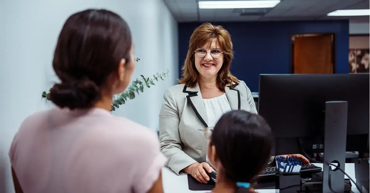 A community bank teller smiling while assisting customers, illustrating how effective IT compliance ensures operational resilience and customer trust.
